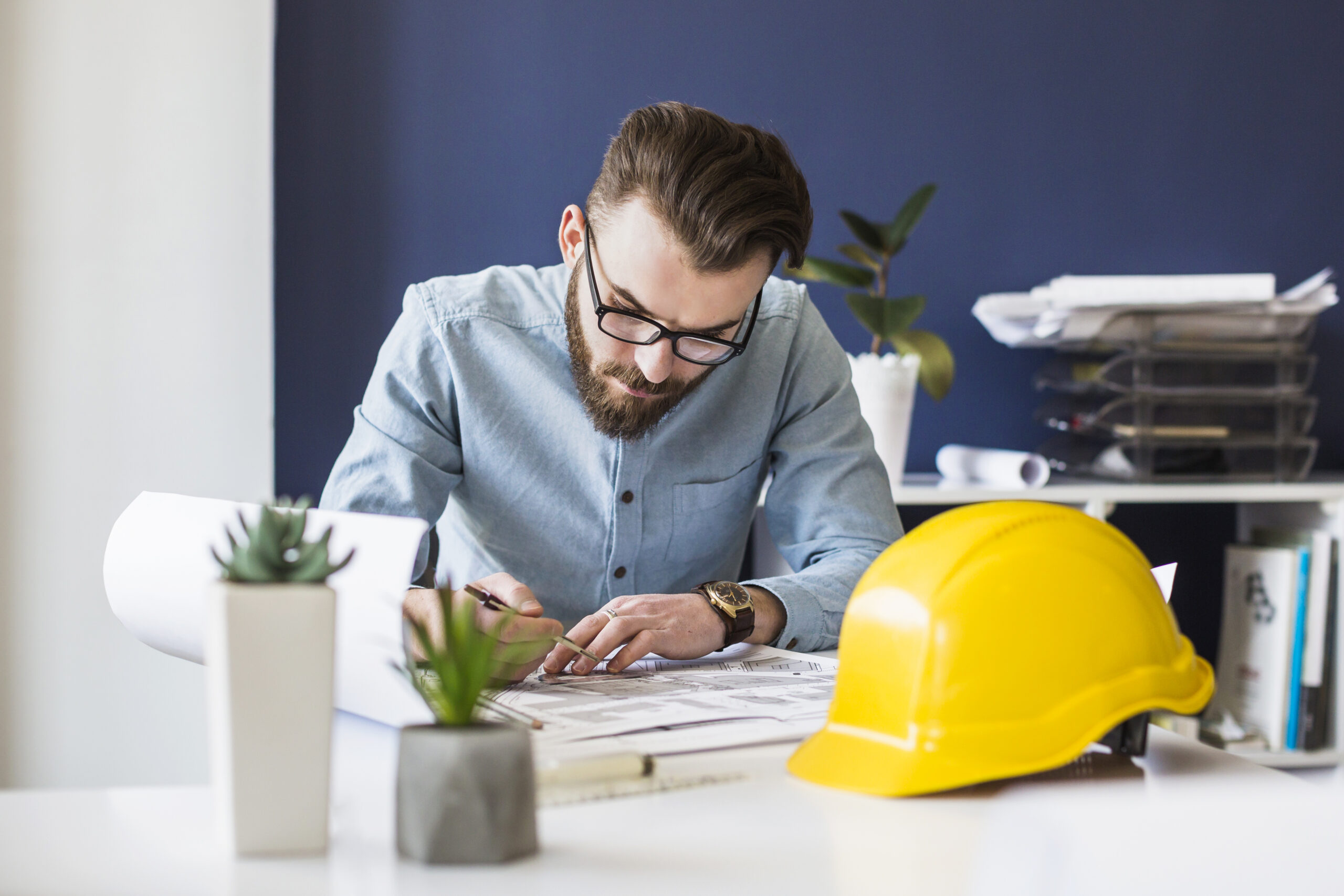 A yellow hard hat is placed nearby, along with potted plants and office supplies.