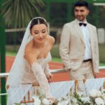 A bride, dressed in an elegant lace wedding gown and veil, gracefully arranges a flower bouquet on a table